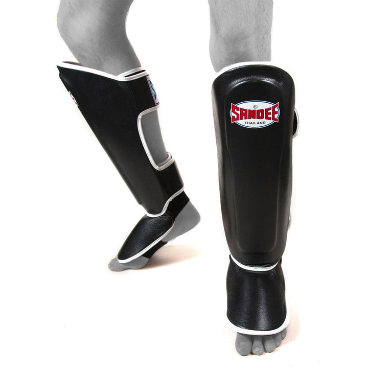 A pair of black and white shin guards with a Sandee logo on the front, designed for adult users.