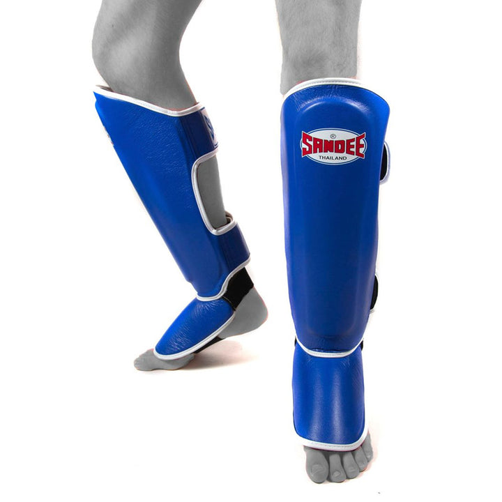 A pair of blue and white Thai shin guards with foot protection, featuring a Velcro closure and contoured design with a Sandee Logo.