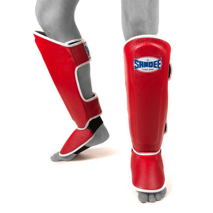 A pair of red and white Thai shin guards with a Velcro strap and a Sandee logo on the front.